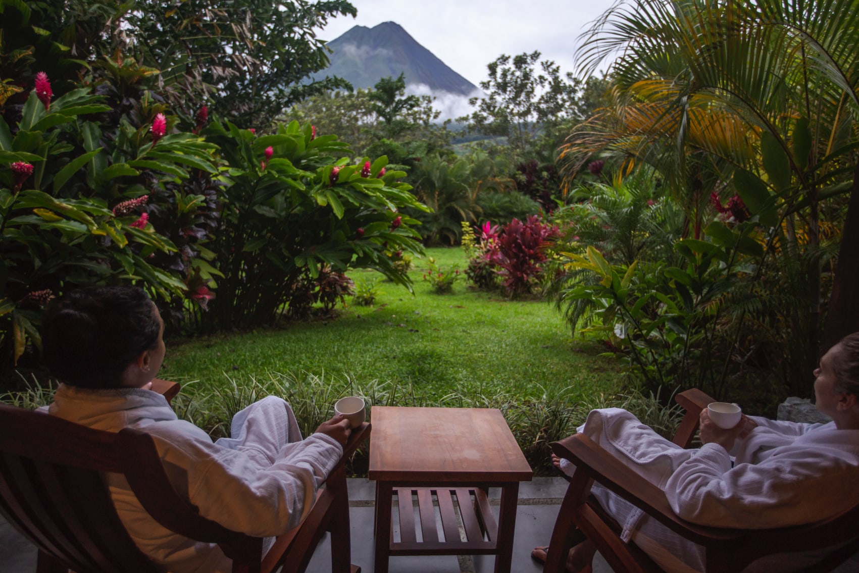 Travellers sharing a sip of coffee and conversation with Arenal in view