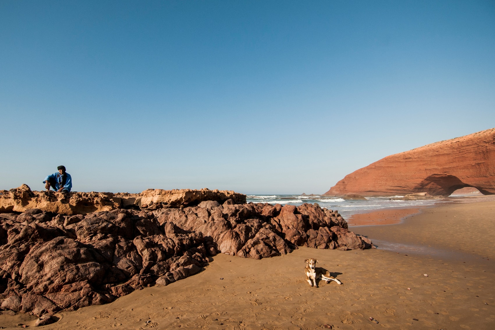 Majestic arch of Legzira Beach with local person and dog