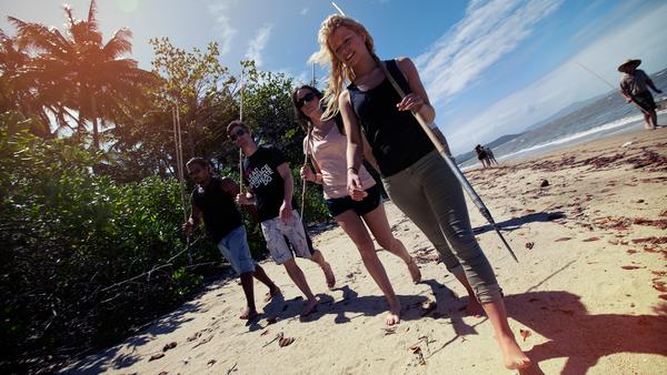 Four tourists walking along a beach in Queensland, Australia with fishing spears