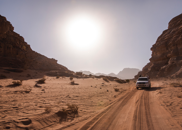 a sturdy 4x4 makes tracks in the desert sands of Wadi Rum as the sun glows on the surrounding canyons