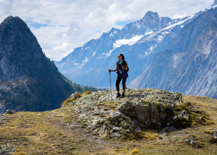 an active female traveller stands with poles in hand in front of the Courmayeur Alps in Italy on the Tour du Mont Blanc